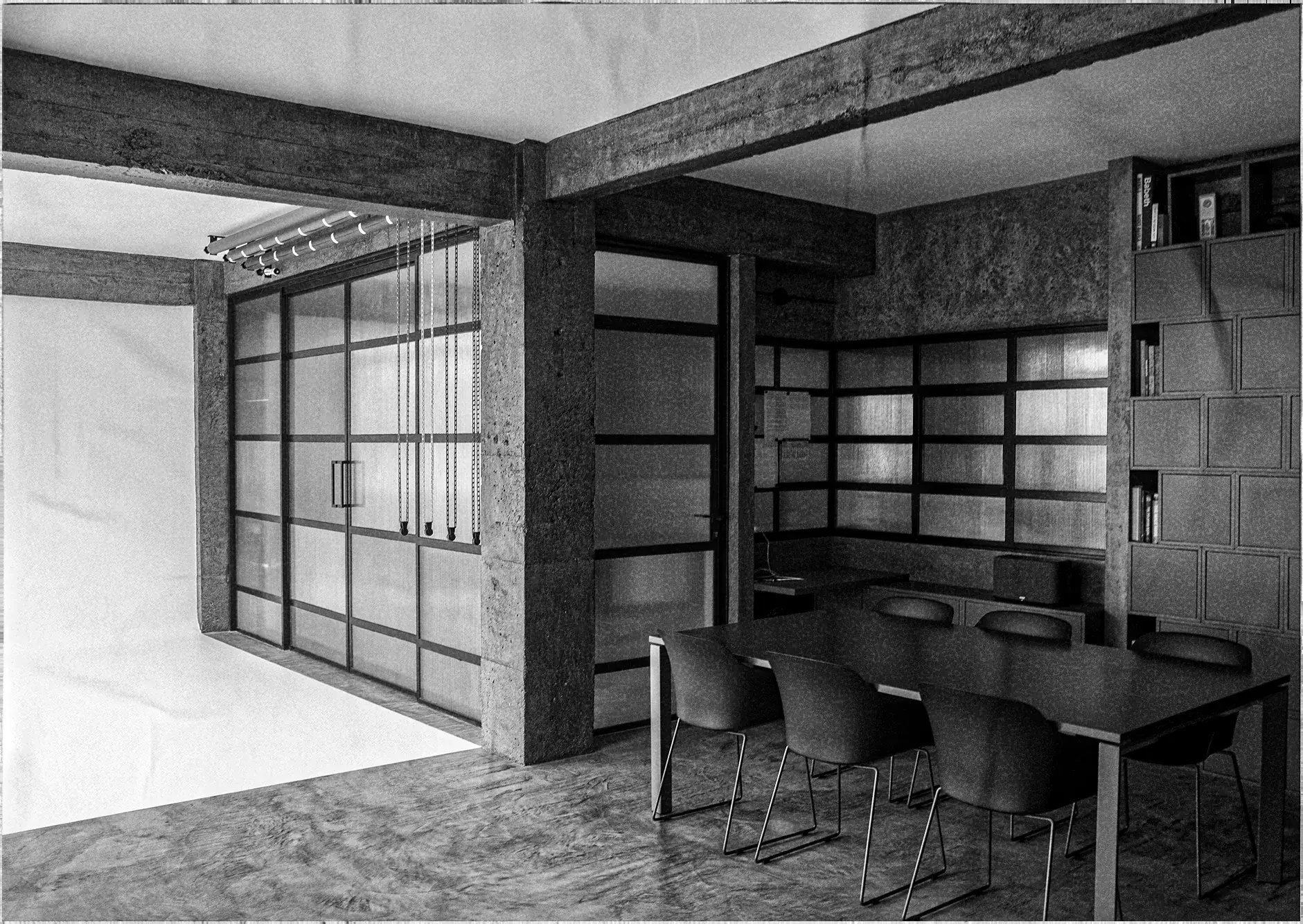 Black and white meeting space in the studio: a table with six chairs, wooden shelving and glass partitions beside the white cyclorama set.