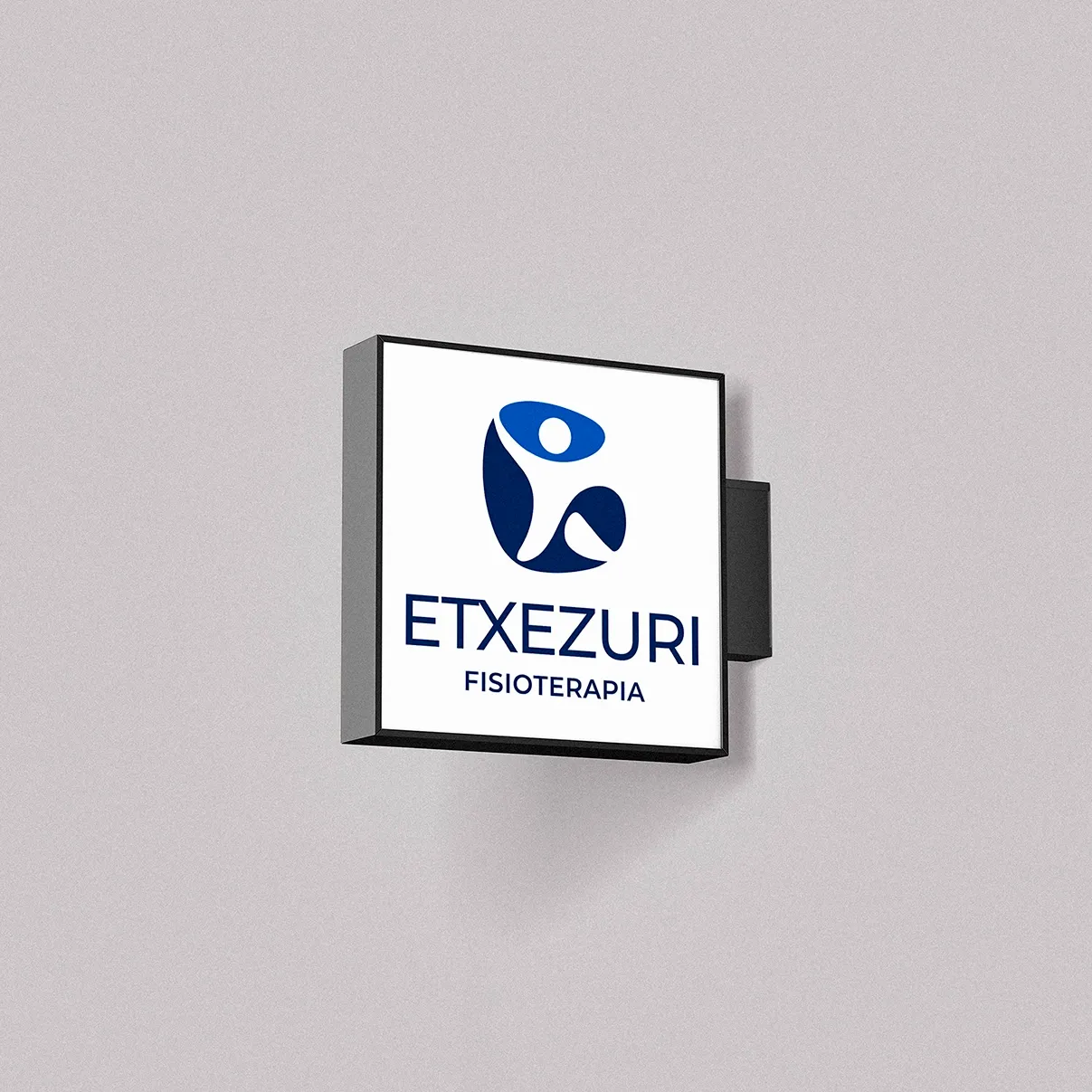 Square illuminated sign for Etxezuri Fisioterapia on a grey facade, with its blue figure logo and navy lettering.