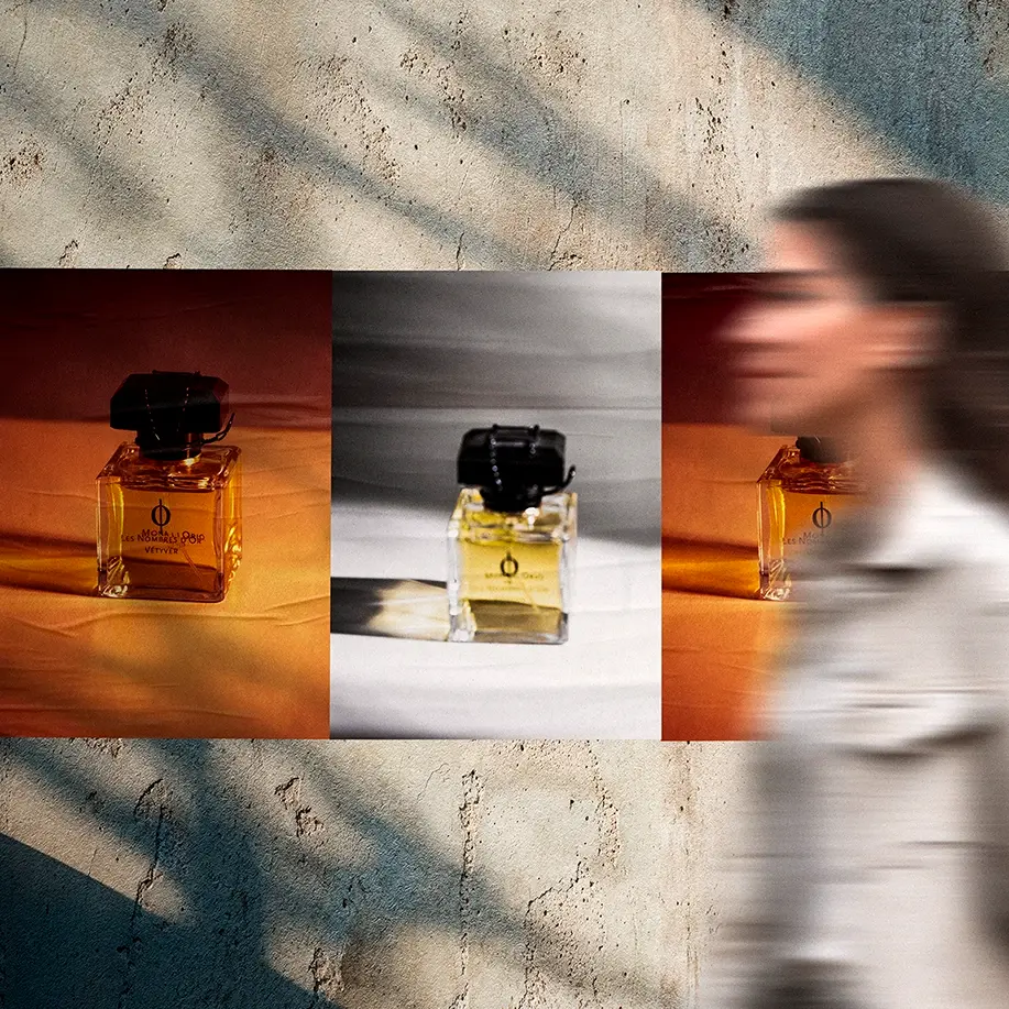 Product photography posters of a perfume bottle in amber and grey tones on a concrete wall, with a blurred woman walking past