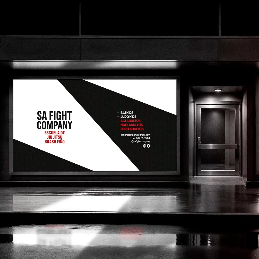 Illuminated storefront window with the SA Fight Company Brazilian jiu jitsu school poster, black and white design listing classes and contact in Bilbao